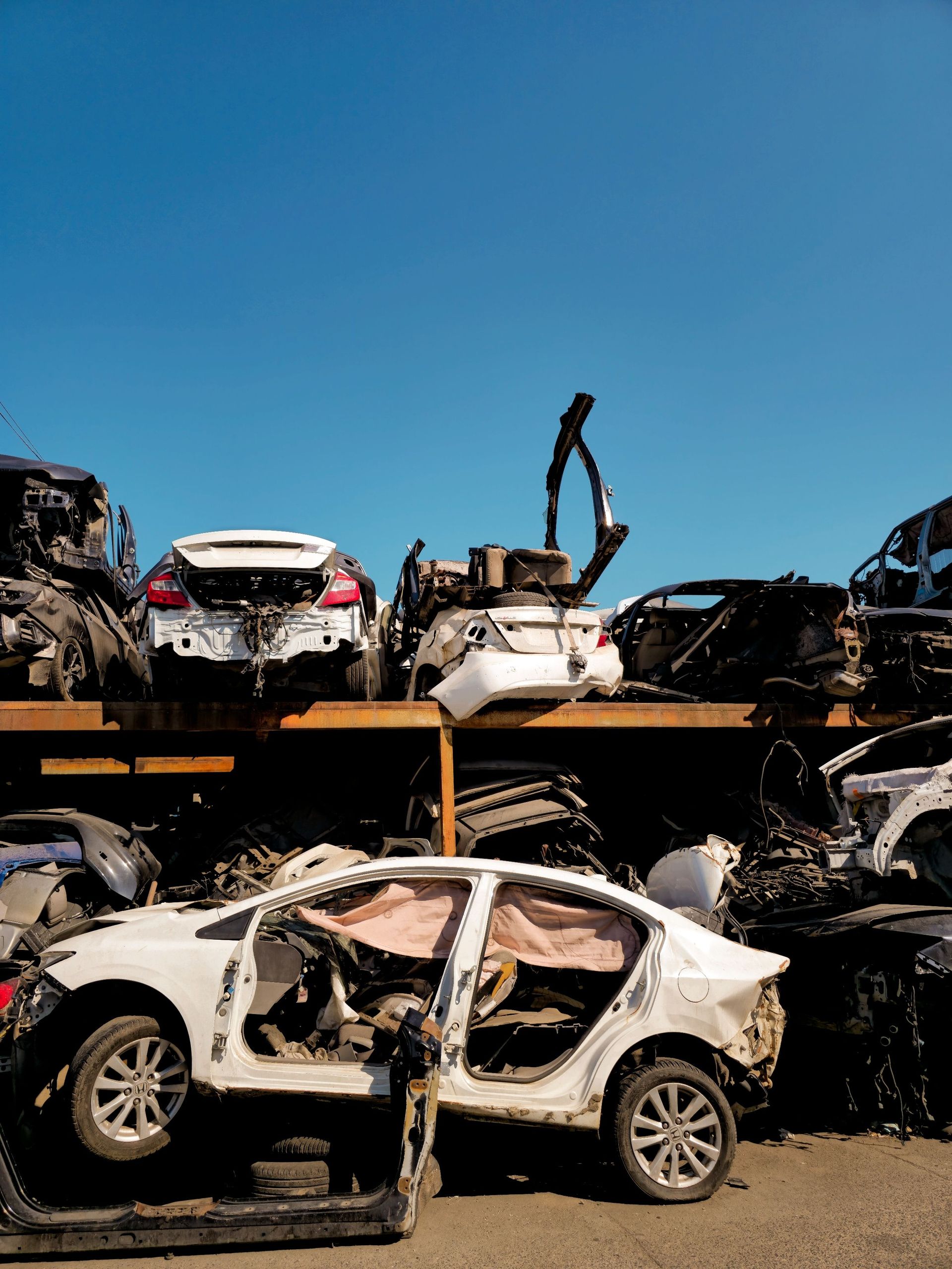 Rows of damaged vehicles in a scrapyard under a clear blue sky.